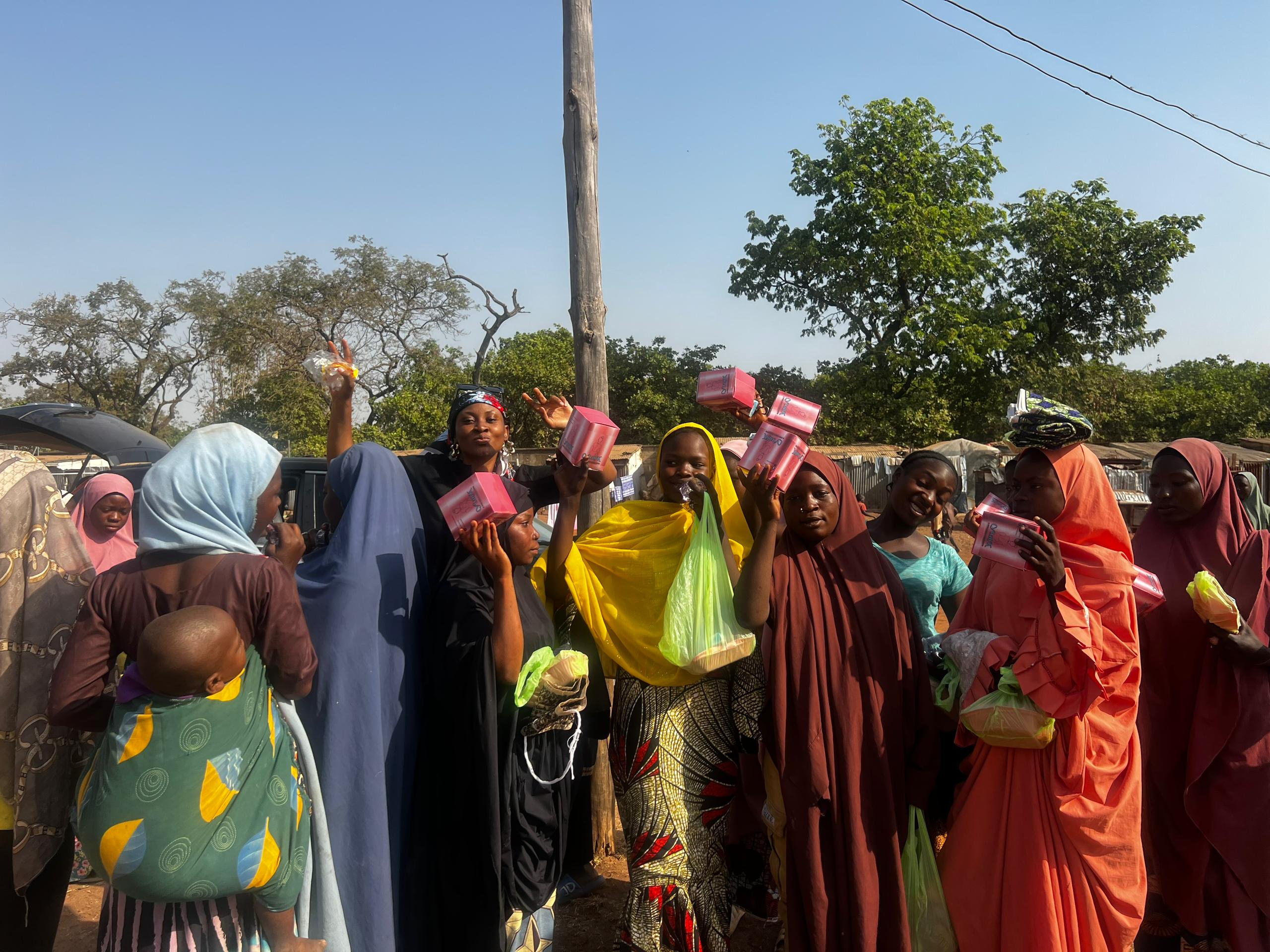 Community distribution day with women and girls holding CyLanK pad boxes